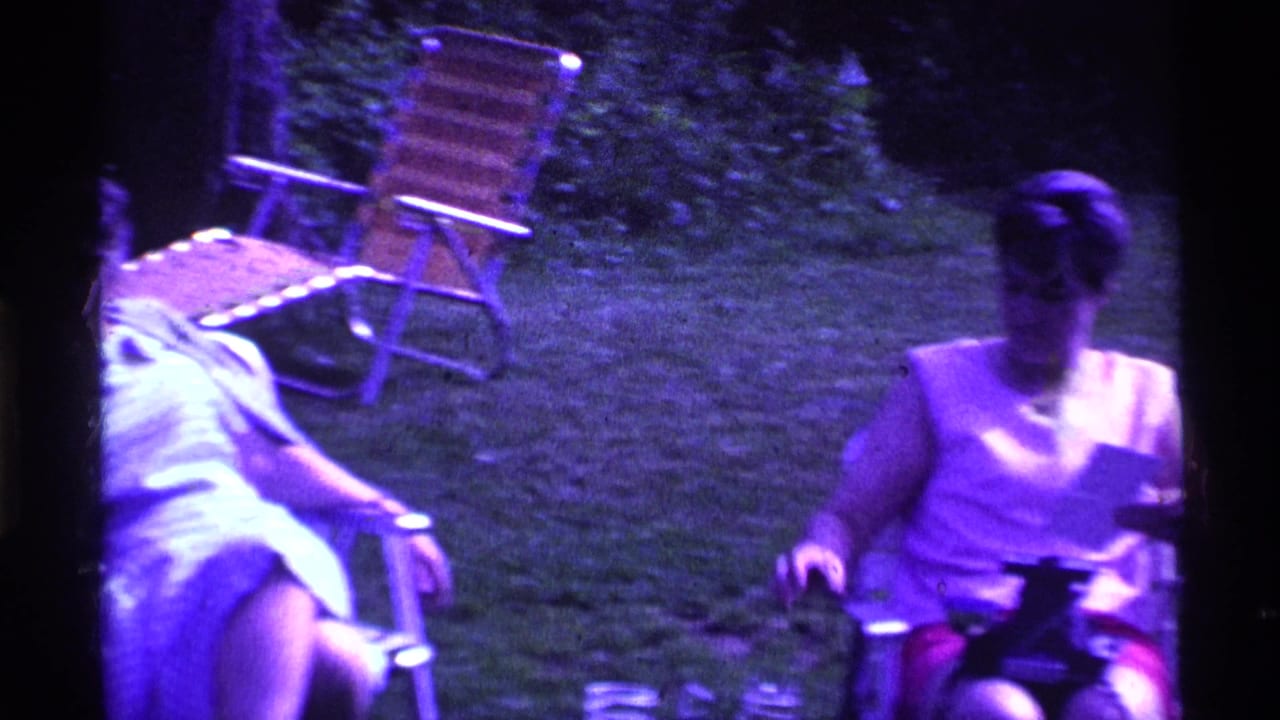 Older women sit in folding lawn chairs on grass under purple-tinted light.