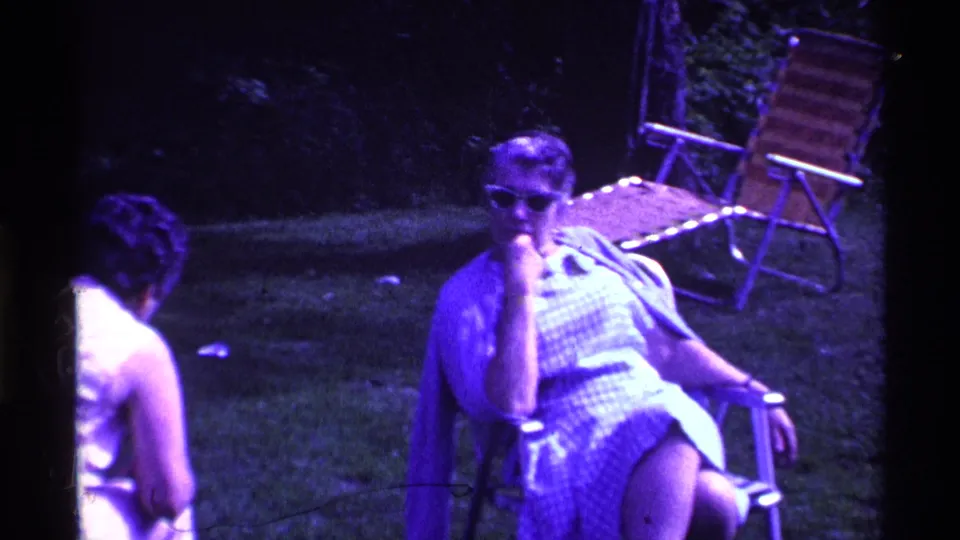 1969 Ohio backyard-style scene with a woman in sunglasses seated in a folding chair and another woman turned away on the grass.