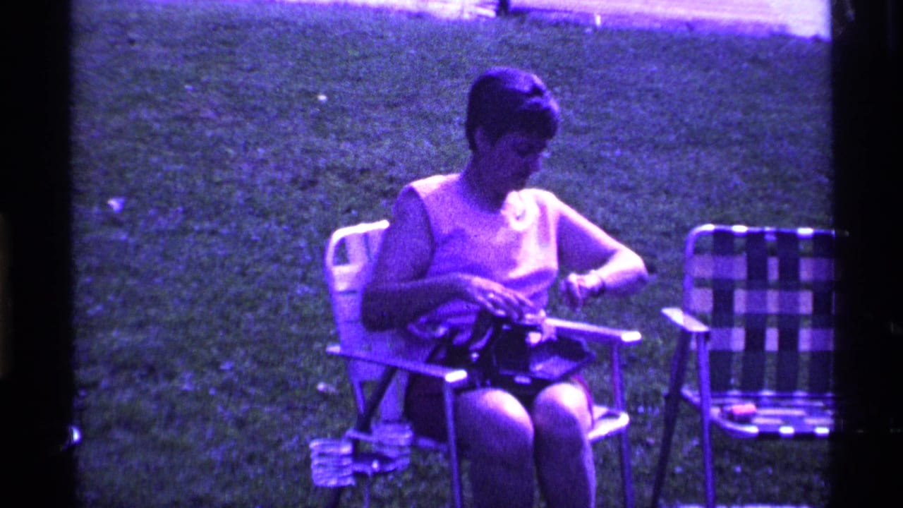 Woman in a sleeveless top looks down while handling a camera on her lap.