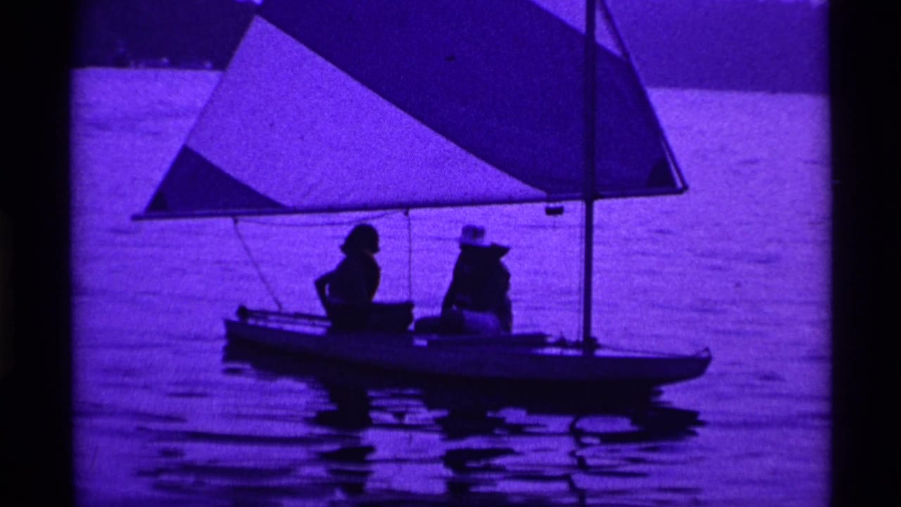 Two silhouetted people sit in a small sailboat on rippled water beneath a triangular sail.