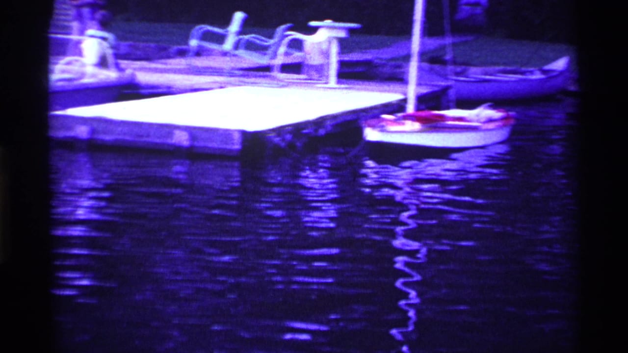 1969 Ohio 8mm frame showing small sailboats near a wooden dock, with lake reflections and a strong purple color shift.