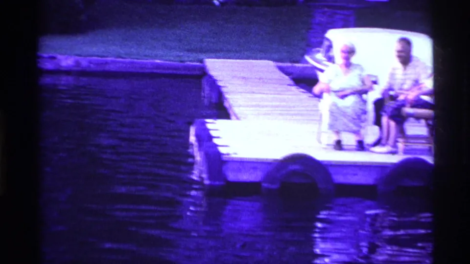 1969 Ohio home-movie frame showing adults relaxing on a wooden dock beside a small boat, partly obscured by the film frame edge.