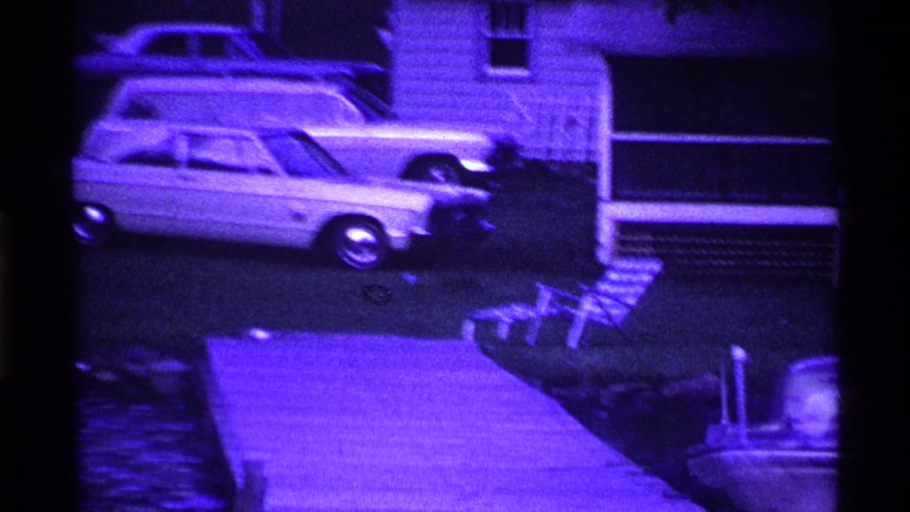 Classic cars parked near a house, with a dock and boat edge visible in the foreground.