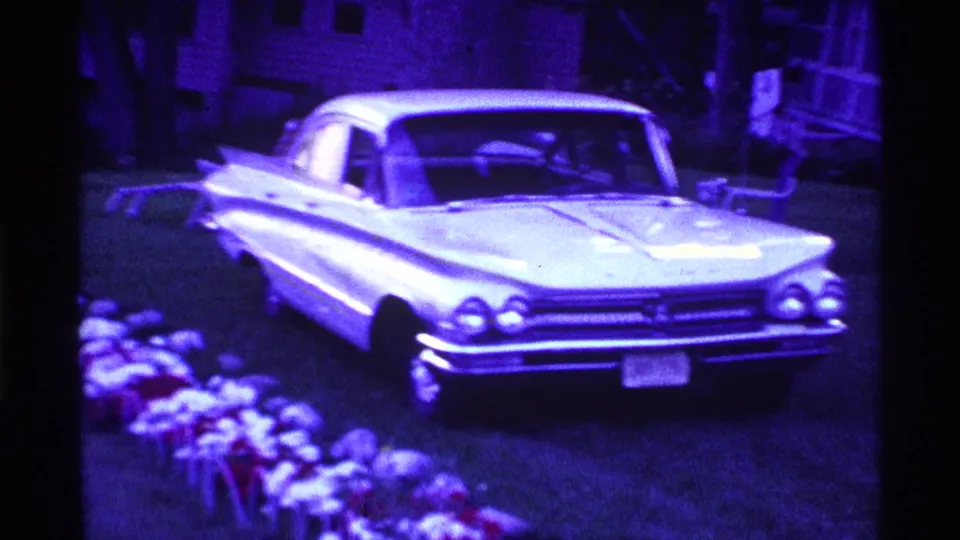 A white vintage sedan is parked near grave-side flowers in this 1969 Ohio home-movie cemetery scene.