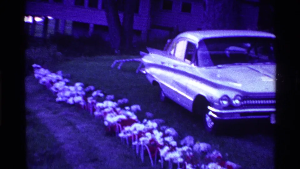 1969 Ohio 8mm frame showing a pale classic sedan on a grassy yard with small objects lined along the lawn.