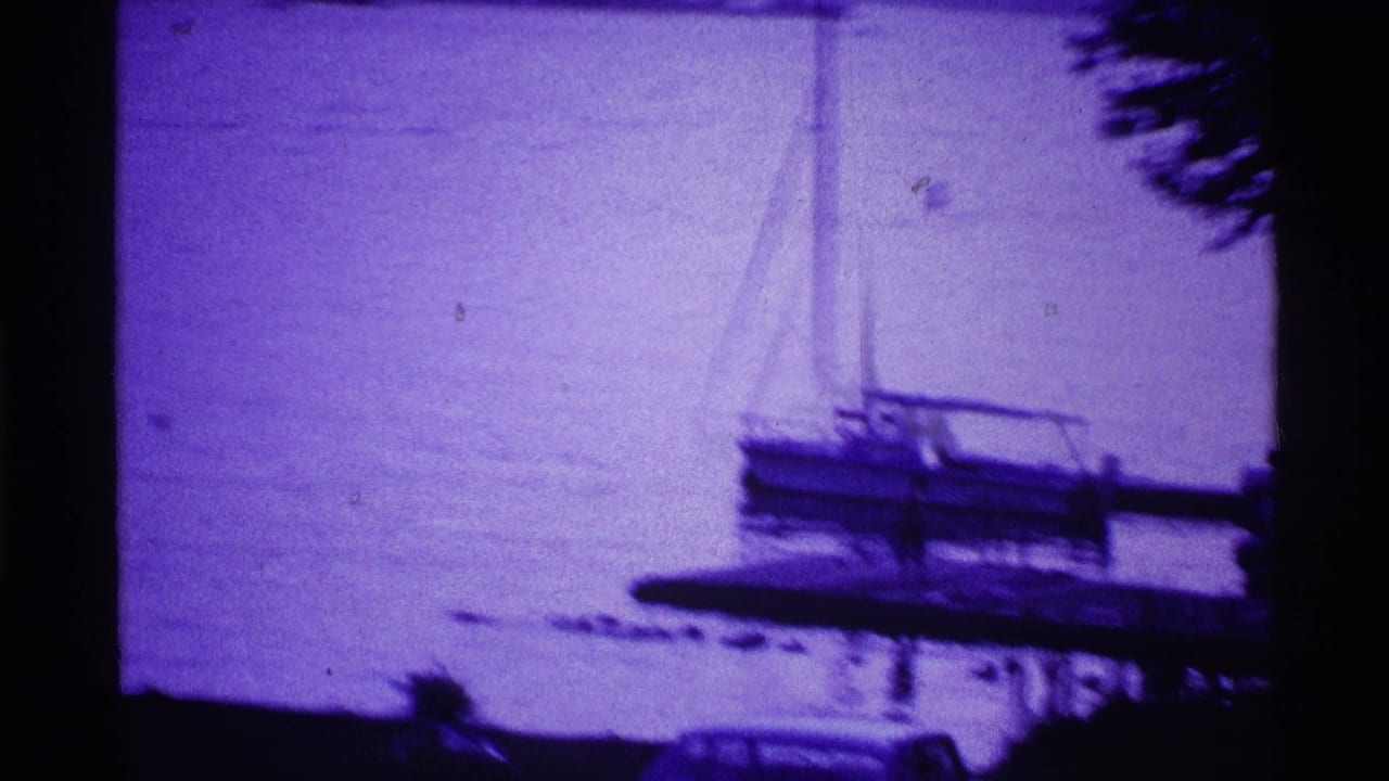 Sailboat near a wooden dock on a lake with dark foreground framing.