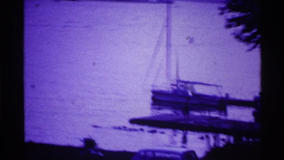 1969 Ohio home-movie frame showing a small sailboat by a lakeside dock, with soft focus and a strong purple film cast.