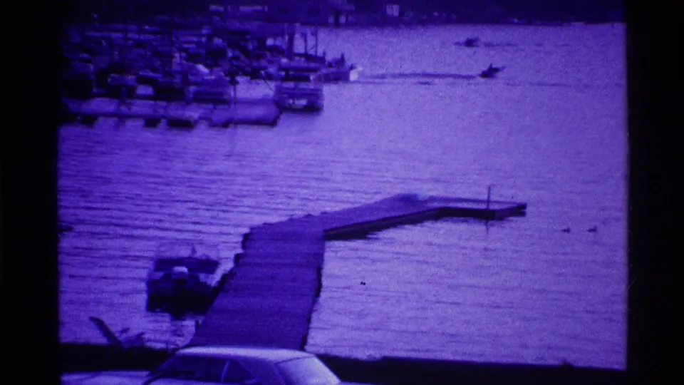 1969 Ohio waterfront view with a wooden dock, small boat near shore, distant marina, and purple-shifted 8mm texture.
