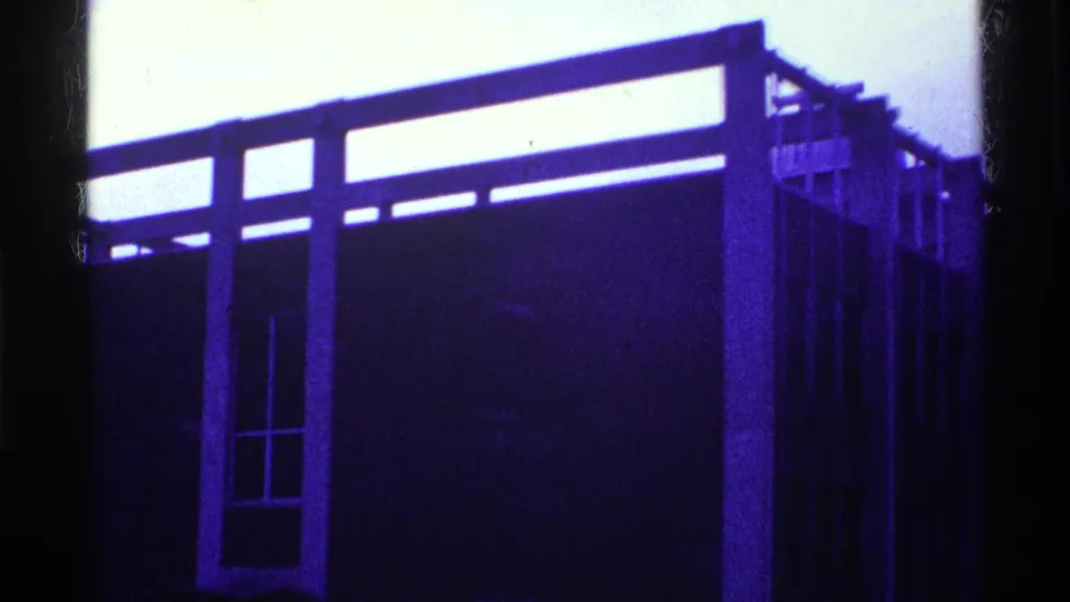 1969 Ohio 8mm frame of a modernist exterior wall with a narrow window bay, upper horizontal structure, and heavy dark framing at left.