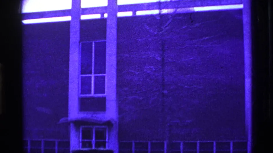 1969 Ohio 8mm frame focused on a blue-tinted facade section with stacked windows, vertical framing, and faint bare branches at right.