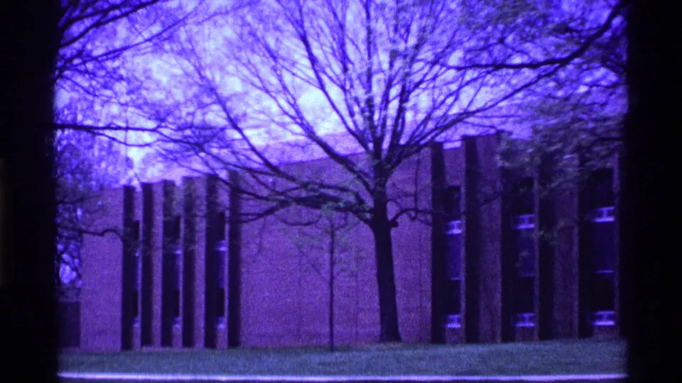 1969 Ohio 8mm frame of a modernist exterior with tall vertical windows, bare trees, grass, and visible home-movie color shift.