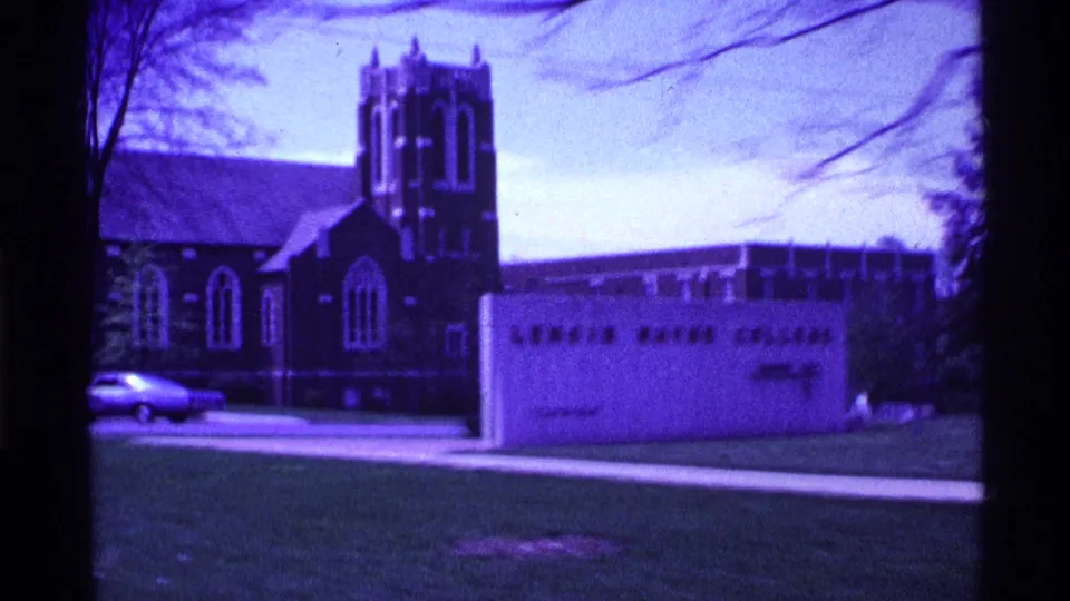 Purple-shifted 1969 Ohio 8mm frame with a visible college sign, brick tower building, parked car, open lawn, and tree branches.