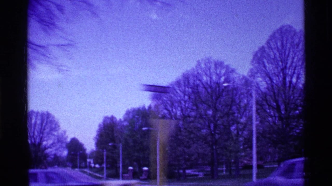 1969 Ohio 8mm frame showing a snow-dusted suburban road, bare trees, streetlights, and a passing car under a purple-blue cast.