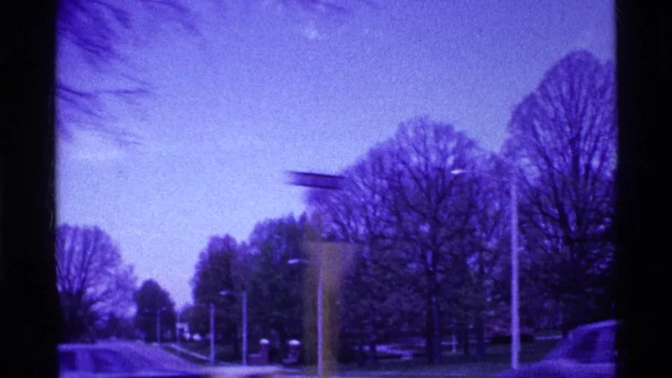 1969 Ohio 8mm frame showing a snow-dusted suburban road, bare trees, streetlights, and a passing car under a purple-blue cast.