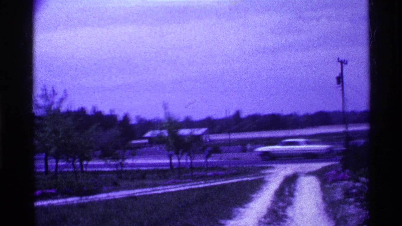 1969 Ohio 8mm frame showing blurred cars on a rural roadside with trees, wet-looking ground, and a utility pole.