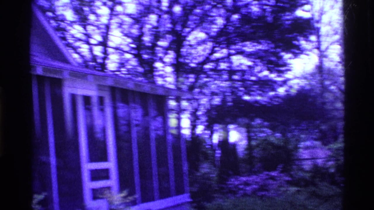 1969 Ohio 8mm frame showing a purple-tinted suburban house exterior with screened porch, trees, and dark film edges.