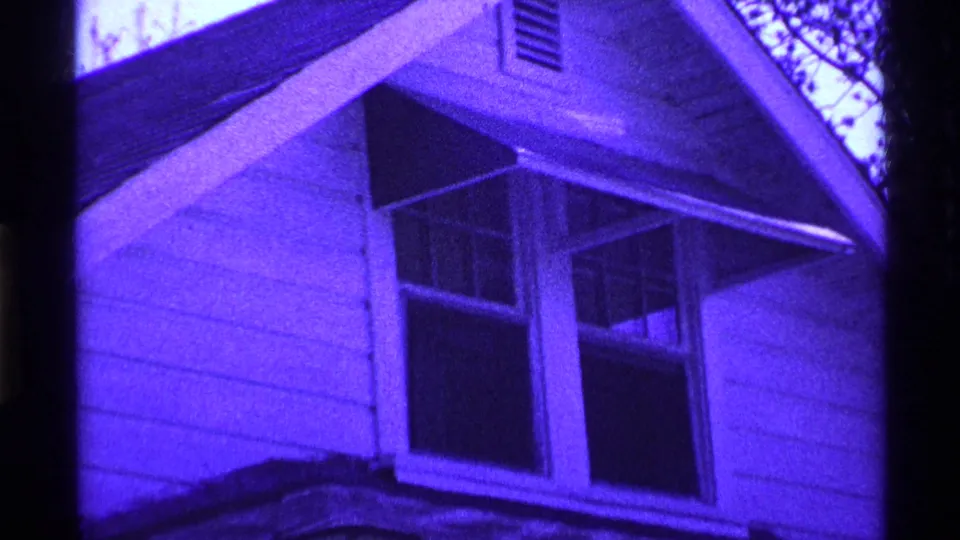 1969 Ohio 8mm frame showing the gabled side of a suburban house with double windows, siding, and roofline in purple tint.