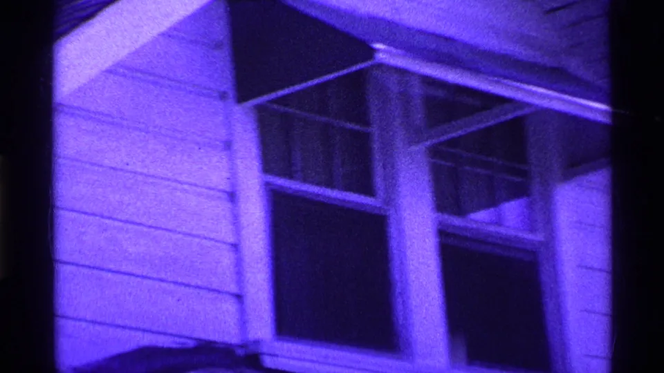 1969 Ohio 8mm frame with close exterior detail of house siding, paired windows, porch supports, and dark window openings.