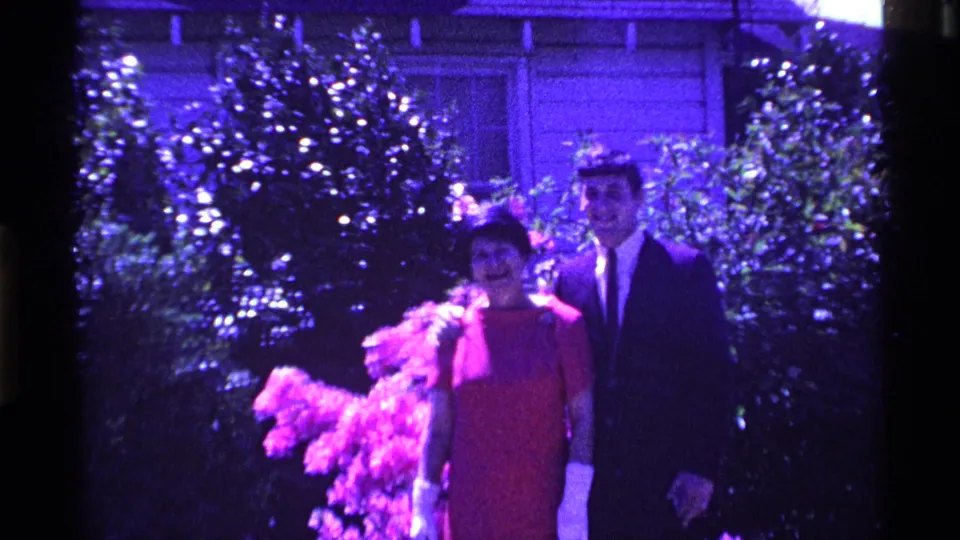 In the 1969 Ohio clip, a woman in a red dress and white gloves stands beside a young man in a dark suit in a backyard garden.