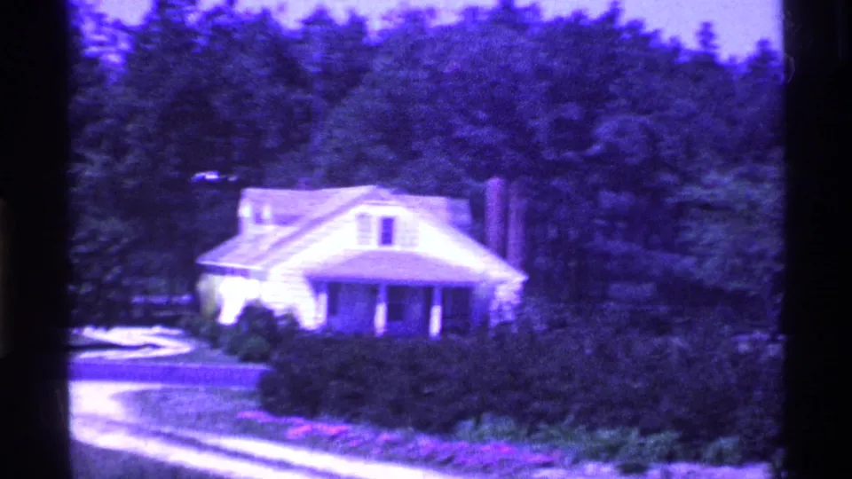 1969 Ohio 8mm frame showing a small white house with porch, shrubs, trees, lawn, and a pale driveway in a purple-shifted scan.