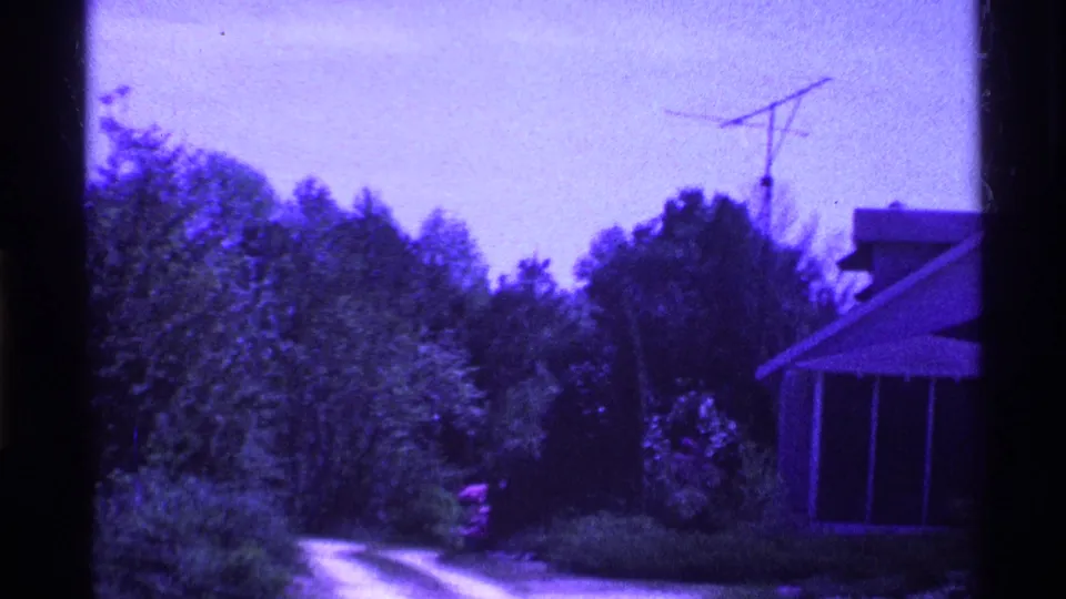 1969 Ohio 8mm frame showing a residential yard with trees, a house edge, roofline, and rooftop antenna.