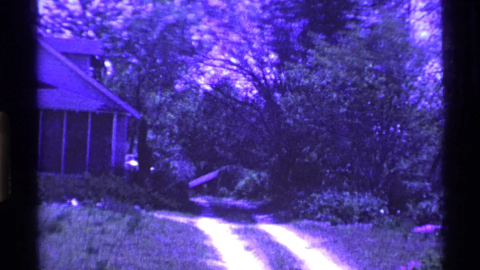 1969 Ohio 8mm frame with the house edge at left and a pale dirt driveway leading through a leafy yard.