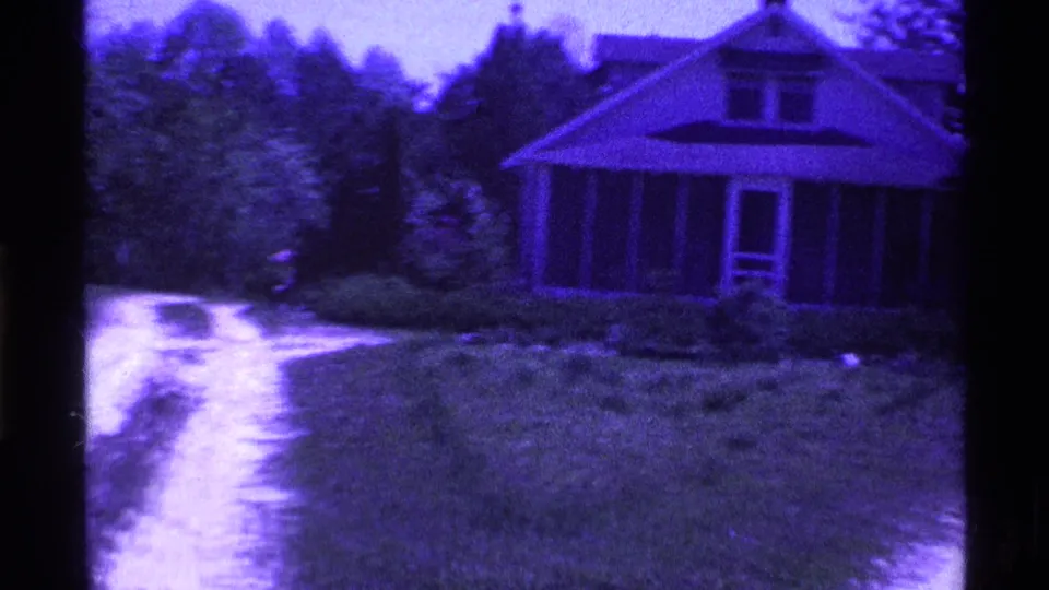 1969 Ohio 8mm frame showing a modest house with a screened porch, front lawn, trees, and a dirt driveway in the foreground.