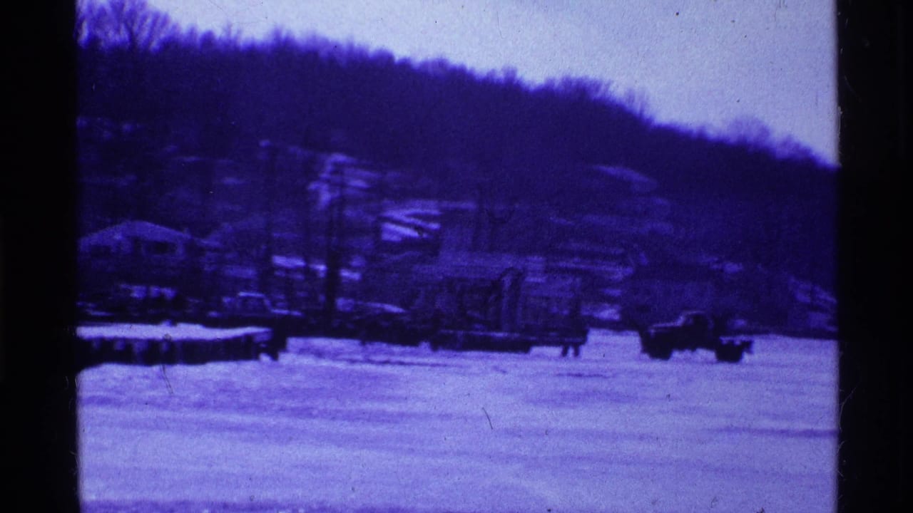 1969 Ohio home-movie frame showing a snowy open area, wooded hillside, bare trees, and small dark shapes in the distance.