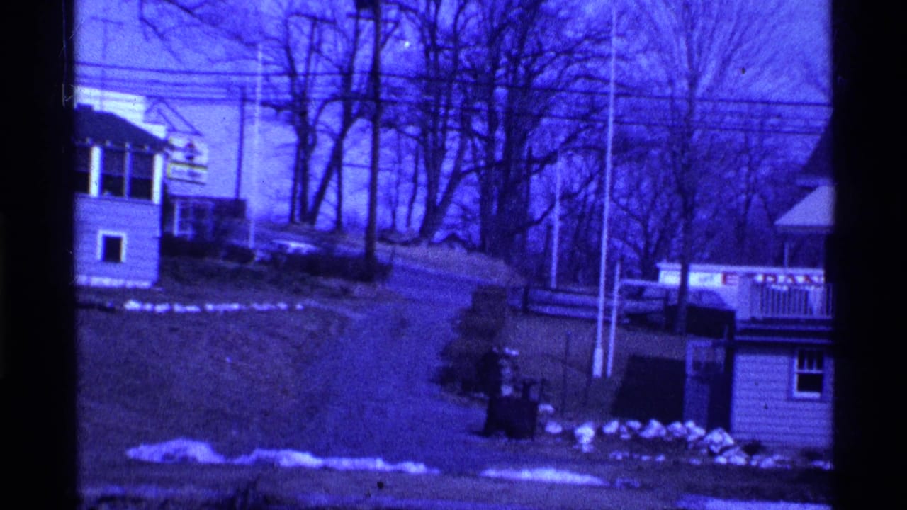 Blue-tinted view of houses on a slope near a frozen lake or snowy ground.