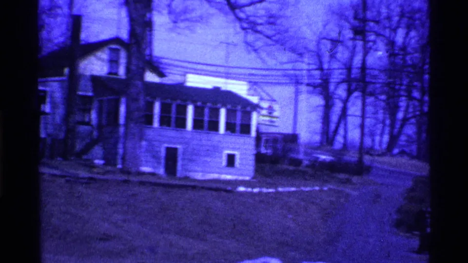 1969 Ohio home-movie frame with a house, yard, bare trees, utility lines, and small snow patches in a winter residential setting.