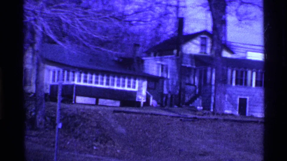 1969 Ohio 8mm frame showing a house with long windows, bare branches, utility lines, and a sloped winter yard.