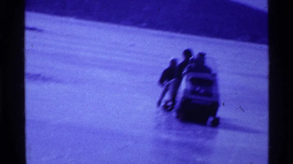 Closer 1969 Ohio 8mm frame showing several riders on a snowmobile crossing a frozen river or lake bed.