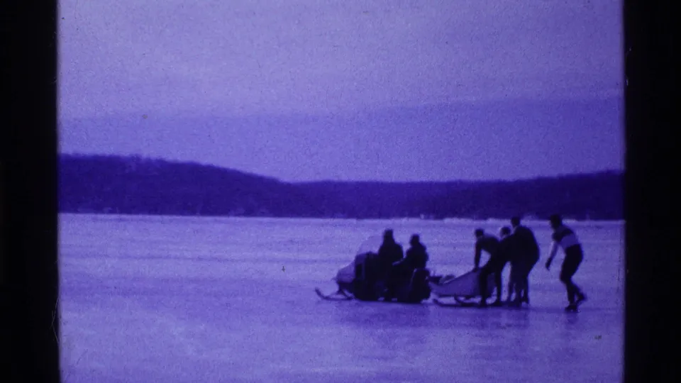 Bundled group on an Ohio frozen lake in 1969, with people pushing or steadying a snowmobile and sled.
