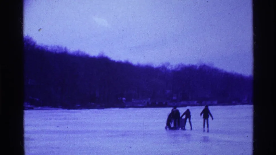 A clustered group and a lone skater appear on the frozen lake, with trees and lakeside structures faintly visible in the distance.