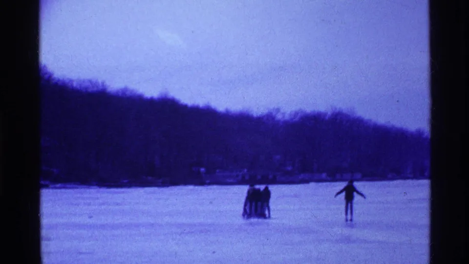 On the frozen Ohio lake, a small group remains together as one skater glides separately across the blue-tinted frame.