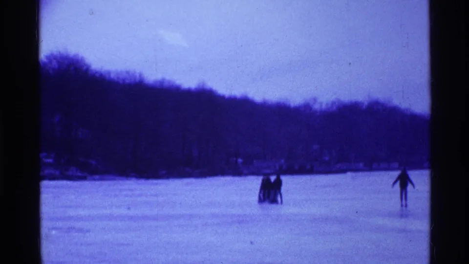 A group of friends and a separate skater remain visible on the frozen lake in 1969 Ohio home-movie footage.