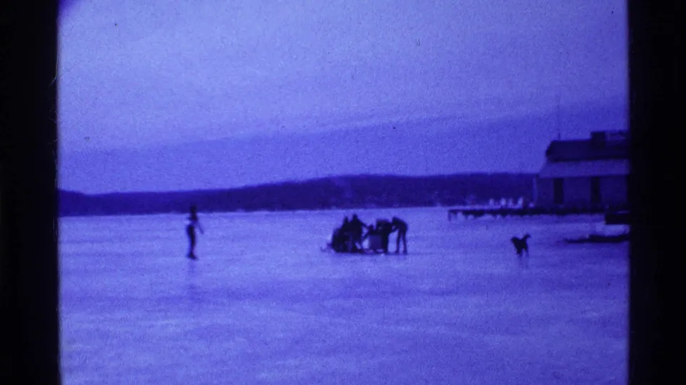 A wider 8mm view shows the sled group and dog spread across the frozen Ohio lake, with a building at the edge of the frame.