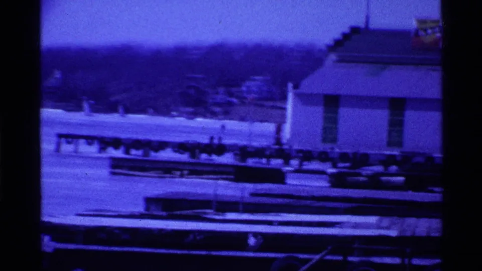1969 Ohio home-movie view of docks, a lakeside building, and frozen water with trees beyond.