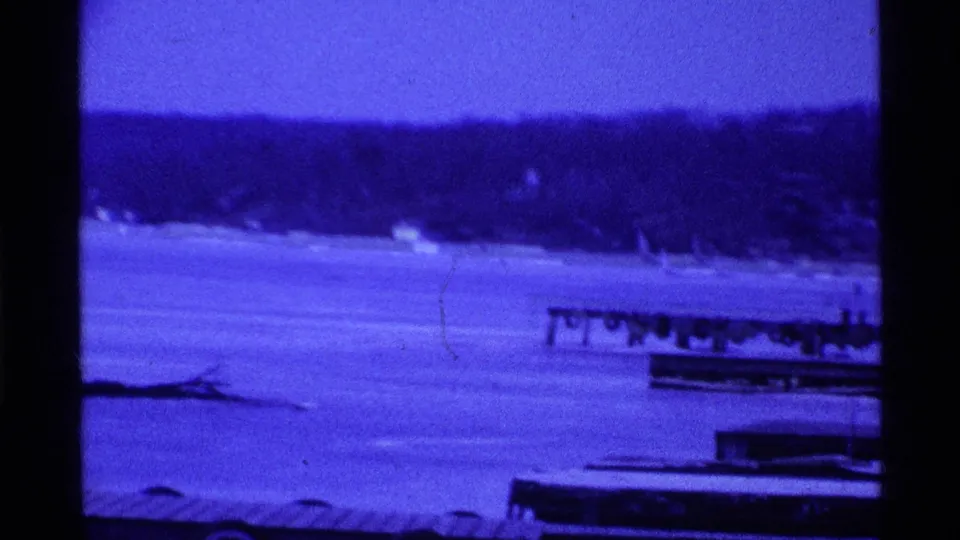 Blue-tinted 8mm winter frame of dock structures on a frozen Ohio lake in 1969.