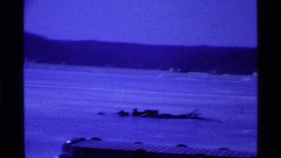 Wide 1969 Ohio winter view across a frozen lake, with shoreline trees and low objects on the ice.