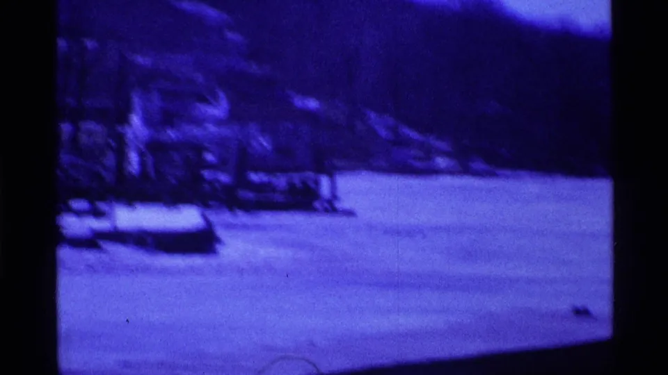 1969 Ohio 8mm frame showing a blue-tinted snowy park or lakeside area with benches, bare trees, and a distant wooded slope.