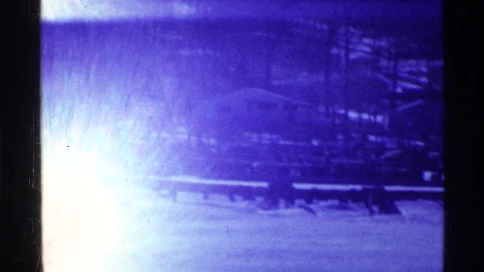 1969 Ohio 8mm frame with strong flare over a snowy park or lakeside view, partially obscuring railings, benches, and trees.
