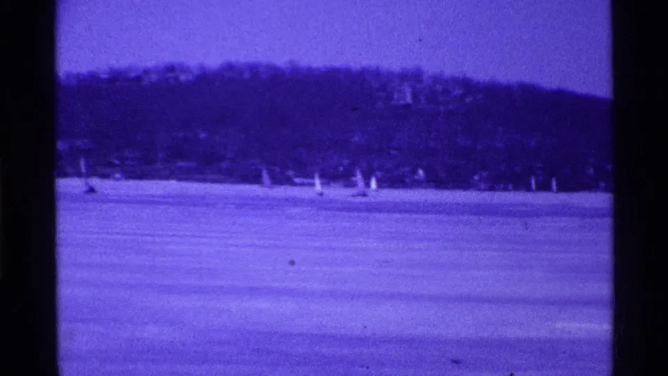 1969 Ohio home-movie frame showing small sailboats on a calm lake below a wooded shore.