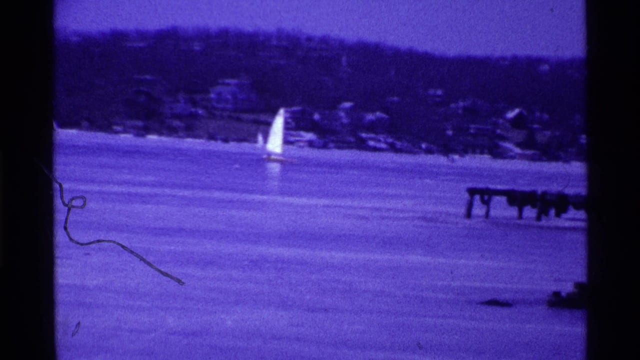 1969 Ohio 8mm frame showing a small iceboat sail in the distance on a frozen lake, with a wooded shoreline behind it.