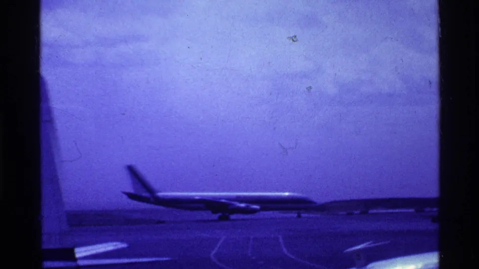 1969 Ohio airport frame showing a passenger jet across the apron, with pavement markings, distant horizon, and purple 8mm color shift.
