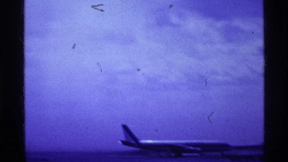 1969 Ohio 8mm frame showing a distant aircraft on a runway under a blue-purple sky, with film grain and frame borders visible.