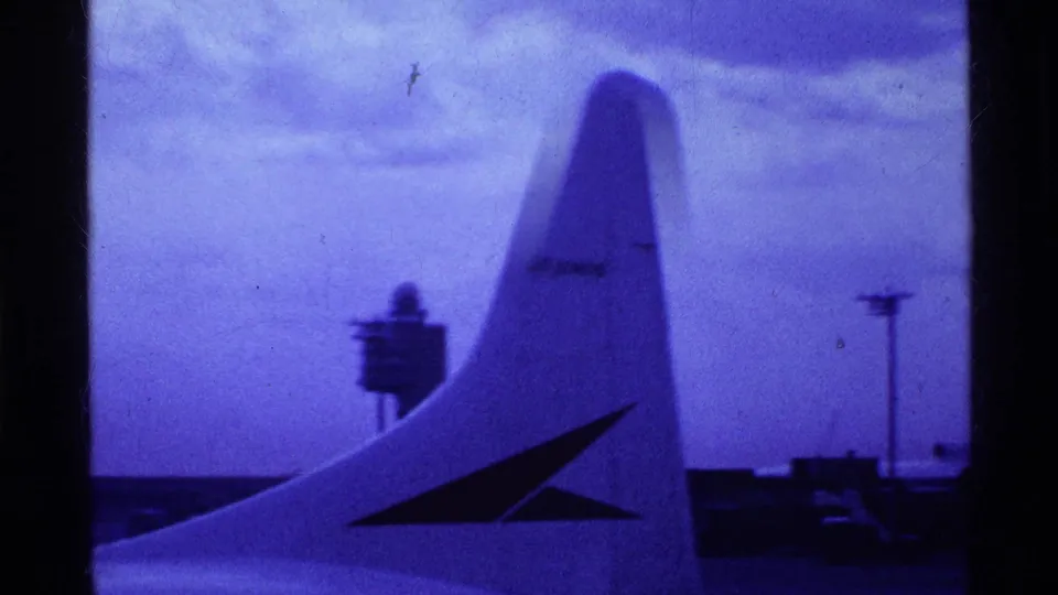 1969 Ohio 8mm frame showing a large aircraft tail or wing surface in the foreground, with runway structures and tinted sky beyond.