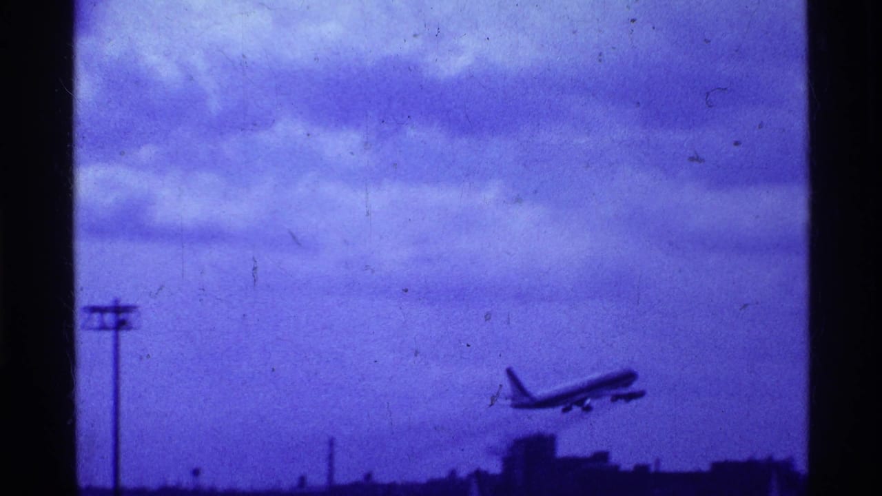 Jet airliner climbing over a dark airport horizon under a blue-purple cloudy sky.