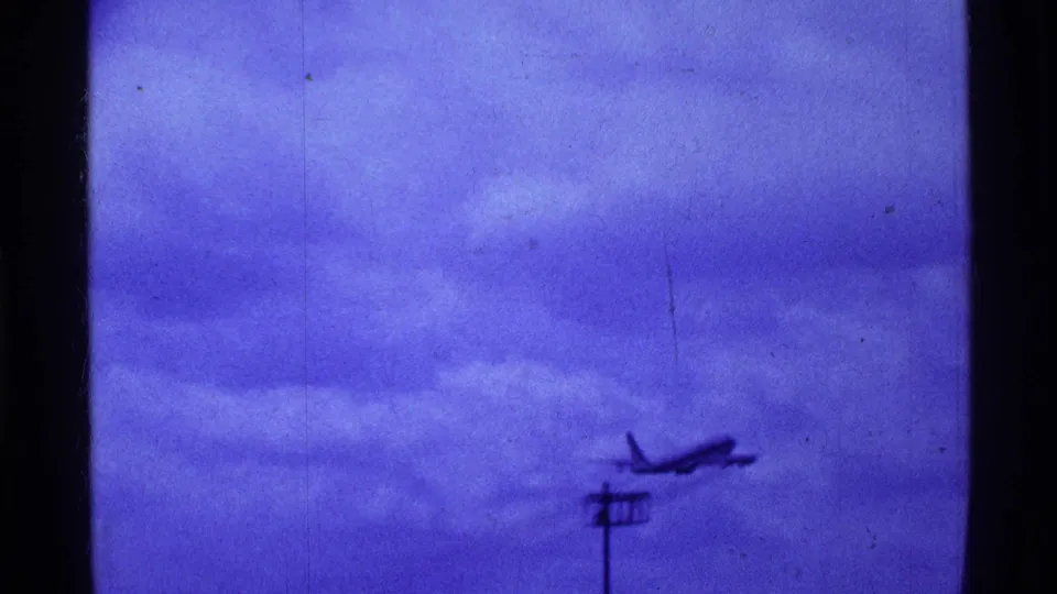 1969 Ohio 8mm frame showing a distant departing jet above a utility pole and low horizon under a blue-purple sky.
