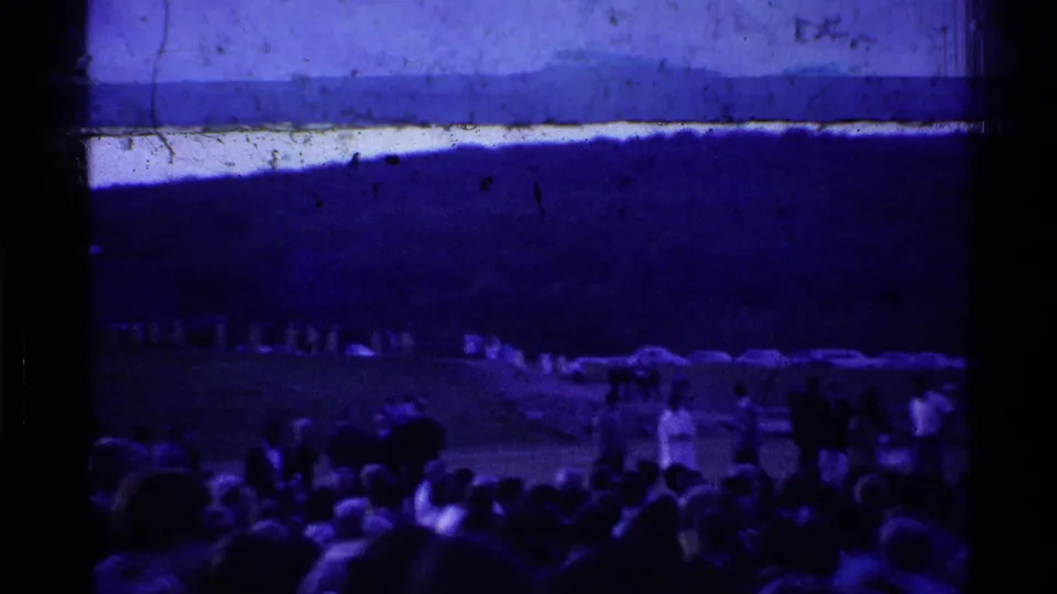 1969 Ohio home-movie frame showing people gathered outdoors near an airfield, watching from below a dark horizon and tinted sky.